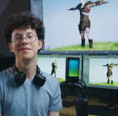 teen in front of computers with game graphics behind him