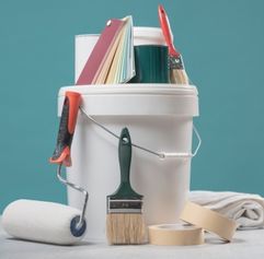 a paint bucked with color samples and rolling pin, tape, paint brush, and tarp