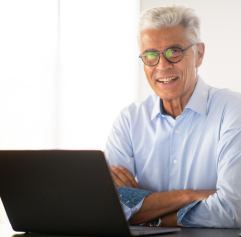 an older person sitting behind a laptop with his arms folded
