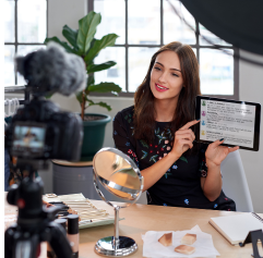 a young woman in front of a camera showing the camera her tablet