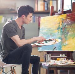 a man sitting on a stool painting an abstract piece