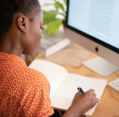 a young woman sitting in front of a computer writing in a notebook