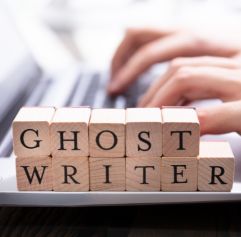 someone typing on a computer and woodblocks that spell out ghost writer in front of him