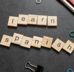 scrabble squares spelling out 'learn spanish' on a chalkboard surface