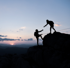 a hiker helping another hiker up a mountain