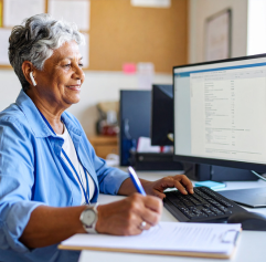 an older woman sitting in front of a computer with a word processor document on it taking notes