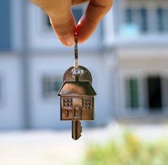 hand holding keys in front of a house