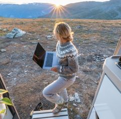 woman holding a laptop looking at the sunset in a mountainous landscape