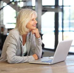 an older woman in front of a computer with her hand under her chin looking into the distance