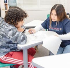 young woman teaching a student Spanish. They are sitting at a desk