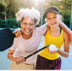 two young girls smiling with a pickleball paddle and ball