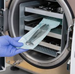 a gloved hand taking out medical equipment from a sterilization machine