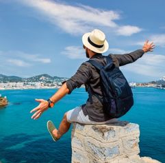 man sitting on a ledge viewing the ocean with open arms