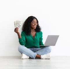 a young woman sitting cross-legged with a laptop on her lap and money in her hand