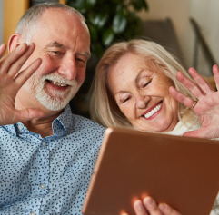 an older couple with a tablet in front of them waiving